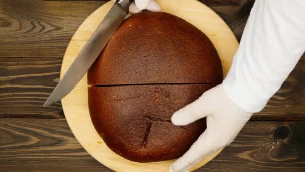 パンのローフを四分の一にスライスします キッチンの板に黒いライ麦パンを切る手 料理は木のテーブルの上でソバパンを切る 粟とふすまから作られた菓子 — ストック動画