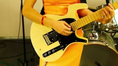 Kız elektro gitar çalıyor. Turuncu elbiseli kadın sanatçı sahnede bir müzik aleti çalıyor. Şarkıcı müzik stüdyosunda sarı elektro gitar çalar. Kadın sahneye çıkmaya hazırlanıyor.