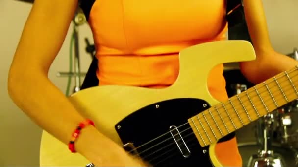 少女はエレキギターを弾く オレンジのドレスを着た女性アーティストがステージ上で楽器を演奏します 歌手は音楽スタジオで黄色いエレキギターを演奏する 女は実行する準備ができて — ストック動画