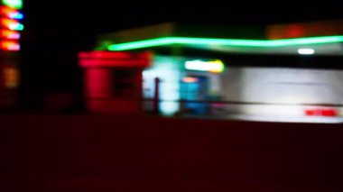 Arabanın camından gece şehrinin bulanık görüntüsü. Parlak renkli ışıkları olan güzel hareketli bir arka plan. Akşam sokakları, aydınlık otoyollar, reklam tabelaları, alışveriş merkezleri ve benzin istasyonları
