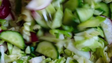 Sebze salatası karıştırıyorum. Vejetaryen salatası, salatalık, lahana, tuz, zeytinyağı. Sağlıklı yiyecekler. Olgun kesilmiş sebze salatası çatalla karıştırılır. Çiftçilerin bahçesinden taze sebzeler