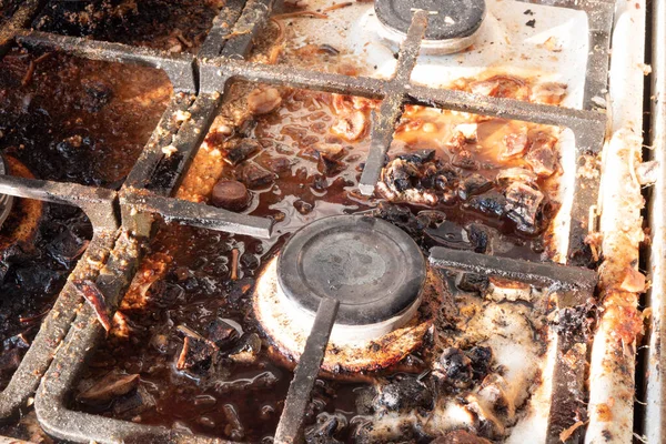 stock image Dirty gas stove surface. Medium gas burner and cast iron grate of a gas oven surrounded by old leftovers of food and drinks. Top area surface and burner heads needs cleaning from burnt-on grease