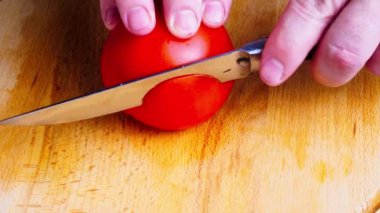 Aşçı elleri tahta tahtada bıçakla taze bir domatesi kesiyor. Yakın çekim. Mutfakta vejetaryen salatası hazırlayan aşçı, 4k görüntü.
