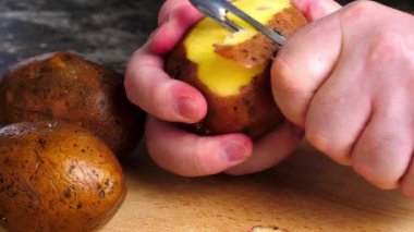 Patates soyan eller. Bir adam patates soyacağı ile tahta kesme tahtasının üzerinde patates soyar. Mutfak masasında sebze soyuyordum. Olgun patates meyveleri yemek pişirmek için hazırlanıyor. Yakın plan.