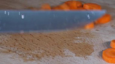 Adamın elleri büyük bir bıçakla tahta bir kesme tahtasının üzerinde havuç kesiyor. Yakın çekim. İnsan keskin bıçak, sağlıklı yemek, ev yemeği, diyet yemeği ve vejetaryen yemekle havucu küçük parçalara ayırıyor..