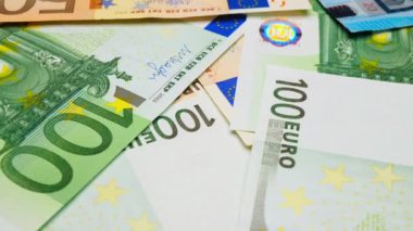 Euro dönüyor. Ağır çekim. Masada 100 Euro 'luk banknotlar dönüyor. Yeni tasarımın kâğıt Euro banknotları taşınıyor. Bir sürü euro faturası. İş anlayışı zenginlik. Mali işler. Ekonomi. Yakın plan.