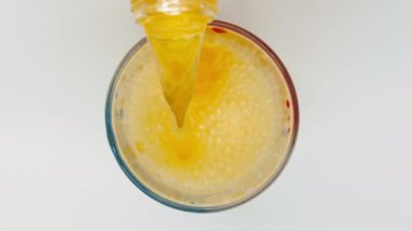 Portakal suyu bardağa doldurulur. Gaz baloncuklu sarı bir sıvı bardağa dökülüyor. Parlak renkli kabarcıklar patlıyor. Beyaz arka planda içki konsepti. Üst Manzara. Yakın plan. İzole edilmiş
