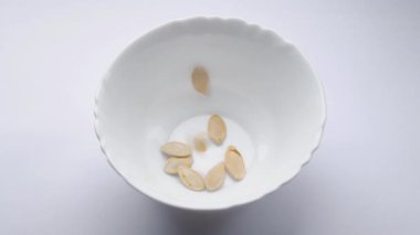 Balkabağı tohumları beyaz arka planda beyaz bir tabağa düşer. Kavrulmuş ve kurutulmuş bej kabak çekirdeği. Büyük sarı kabak çekirdekleri. Sağlıklı yiyecekler. Vejetaryen yemeği. Vejetaryenler için yemek. Yakın plan. Üst görünüm
