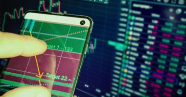 İş adamı haritayı akıllı telefonunda finans mumlarıyla kontrol eder. İş haberleri arka planda bilgisayar ekranında, finansal özgürlükle.