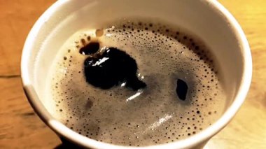 Kahve damlası, siyah arka planda köpük, yiyecek ve içecek ve rahatlama konseptiyle bir fincan espresso italyan kahvesinin içinde süper yavaş çekimde düşüyor.