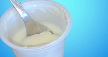 Kaşık beyaz yoğurt kavanozuna batıyor, mavi arka planda konsept, sağlıklı yiyecek konsepti ve