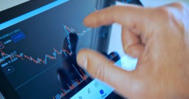 İş adamı tabletindeki mali mum grafiğinde çimdik attı. İş haberleri arka planda bilgisayar ekranında, finansal özgürlükle ilgili.