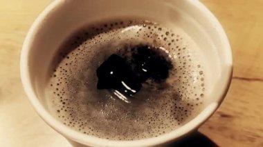 Kahve damlası, siyah arka planda köpük, yiyecek ve içecek ve rahatlama içeren bir fincan espresso italyan kahvesinin içinde süper yavaş çekimde düşüyor.
