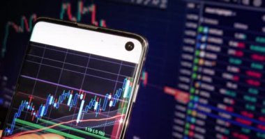 İş adamı haritayı akıllı telefonunda finans mumlarıyla kontrol eder. İş haberleri arka planda bilgisayar ekranında, finansal özgürlükle.