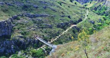 Matera 'da tatil, Gravina di Matera' da yürüyün. Arka planda taşlar ve Gravina 'yı geçen tibet köprüsü, açık mavi gökyüzü altında, doğa kavramı, kültür