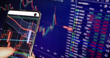 İş adamı haritayı akıllı telefonunda finans mumlarıyla kontrol eder. İş haberleri arka planda bilgisayar ekranında, finansal özgürlükle.