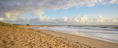 Sabahın erken saatlerinde Cotton Tree plajında bulutlu bir gökyüzünü, dalgaların akışını, popüler bir kumlu sahili ve erozyona karşı korunmak için deniz kenarı ya da Groyne inşa eden kum dolu konteynırları görüyoruz.