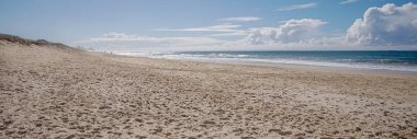 Seascape landscape panoramic view of sandy beach, ocean and straight horizon with lots of footprints in the sandy foreshore clipart