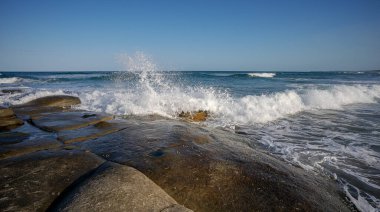 Sörf dalgaları, Point Cartwright, Kawana, Queensland 'daki kayalık burnun kıyısındaki büyük kaya platformunda süzülürken beyaz köpüklü su sıçrıyor. 