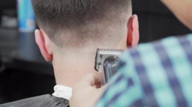 Bu dinamik sahnede, bir berber bir kırpıcıyı ustalıkla kullanır, erkek müşterilerinin kafalarının arkasını titizlikle şekillendirir. Berberin canlı ve kareli gömleği temiz olanla çok güzel zıtlaşıyor.