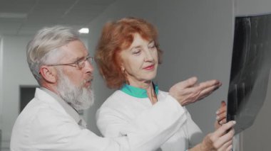 Modern bir hastane ortamında, yaşlı bir kadın doktor erkek meslektaşıyla MRI taramasını incelerken odaklanmış bir tartışmaya girer. İfadeleri derin bir konsantrasyonu yansıtıyor ve...