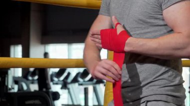 Kesilmiş bir atış kararlı bir erkek boksörü yakalar. Canlı kırmızı bilek bandajları uygular ve spor salonunda yapılacak güçlü bir antrenmana hazırlanır. Bu görüntü özgüven ve adanmışlık yayıyor.