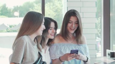 Üç neşeli genç kadın şık bir kahve dükkanında neşeyle selfie çekiyorlar. Kahkahaları havayı dolduruyor. Parlak doğal ışık ve rahat bir ortam ile çevrelenmiş bir şekilde kutluyorlar.