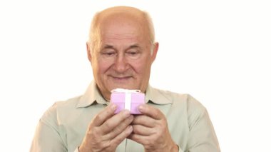 Mutluluk ve sıcaklık saçan, zarif bir şekilde paketlenmiş bir hediye kutusunu tutarken neşe saçan, gri saçlı, neşeli yaşlı bir adam. Bu iç açıcı sahne kutlamanın özünü yansıtıyor, aşkım.