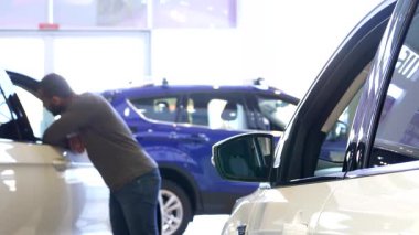 Şık bir siyah adam galeride parlak bir arabayı incelemek için öne eğilir, camdaki yansıması görülebilir. Bu genç, sakallı Afrikalı Amerikalı müşteri düşünceli bir şekilde...