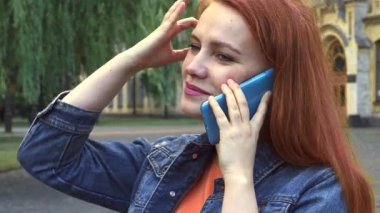 Zeki telefonuyla neşeli bir sohbetin tadını çıkaran neşeli kızıl saçlı bir kızın yakın plan bir üniversite kampüsünün pitoresk zeminine kurulmuş hali. Onun ışıltılı gülümsemesi ve kahkahası saf mutluluğu yansıtır