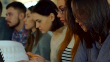 Çekici bir kız öğrenci yüzünü kameraya çeviriyor ve hareketli bir konferans salonunda ışıltılı gülümsemesini sergiliyor. Bu yakın çekim gençlik merakı ve akademik adanmışlığın özünü yansıtıyor.