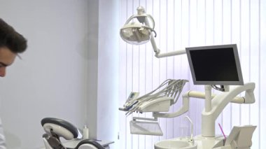 Kendine güvenen, yakışıklı sakallı bir dişçi şık diş muayenehanesinde gururla durur. Kollarını kavuşturur ve sıcak bir şekilde gülümser. Çekici beyaz doktor uzmanlığını ileri düzeyde bir arka planda sergiliyor.