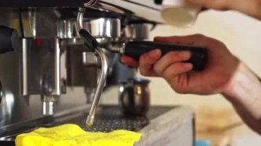 Yetenekli bir barista ustalıkla zengin bir fincan kahve hazırlar, kahve makinesi arka planda mırıldanırken taze demlenmiş içeceğe şurup döker. Odaklanmış elleri sanatını sergiliyor.