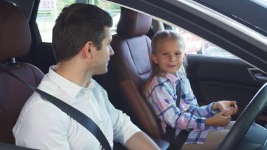 Gösterişli bir arabanın içinde, koyu saçlı genç bir baba büyüleyici bir menekşe elbise giyen küçük kızıyla hoş bir sohbete girişiyor. Onların sıcak değişimi sevgi ve bağlılık yayar.