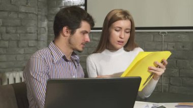 Şık sakallı, odaklanmış genç bir işadamı, zarif bir dizüstü bilgisayarın yanında canlı sarı belgeler tartışan nazik bayan meslektaşıyla yakınlaşıyor. Bu sahne özünü yakalar.