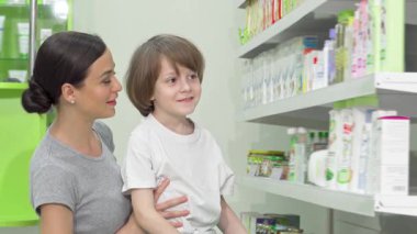 Neşeli bir anne küçük oğlunu hareketli bir eczanede sergilenen renkli ürünleri keşfederken kucaklıyor. Ortak merakları ve bağlantıları aile zamanlarının sıcaklığını vurguluyor.