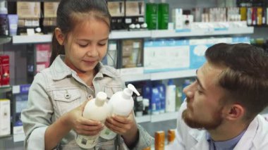 Uzun siyah saçlı hoş bir kız elinde iki şişe kozmetik ürünüyle, bakımlı sakallı, arkadaş canlısı bir eczacının tavsiyesini bekliyor. Sıcak gülümsemeleri ve çekicilikleri