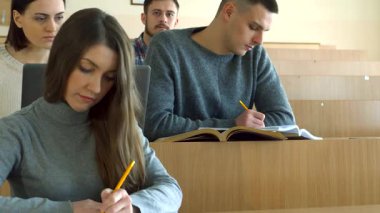 Parlak bir konferans salonunda, genç beyaz öğrenciler egzersiz kitaplarına notlar yazmakla derinden meşguller. Güzel bir esmer kız ve yakışıklı bir adam, ikisi de gündelik giyinmiş, kalemleri sıkıca tutuyorlar.