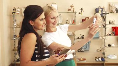 Bir esmer ve sarışın arkadaşı hoş bir alışveriş deneyimine dalmış, sandaletleri bir selfie ile karşılaştırırken. Bir dizi modaya uygun ayakkabıyla çevrili.