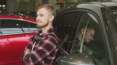 Şık sakallı bir adam modern bir bayilikte parlak bir arabaya yaslanmış, parlak bir gülümsemeyle başparmağını kaldırıyor. Bu canlı sahne bir araç satın almanın heyecanını yakalıyor.