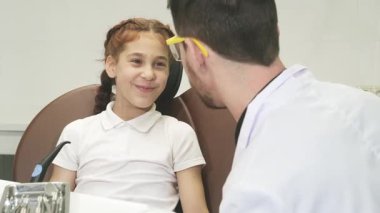 Parlak bir diş muayenehanesinde, örgülü siyah saçlı sakin küçük bir kız, dişini göstererek, acısını dost canlısı bir erkek dişçiyle tartışır. Güven verici atmosfer onun cesaretini vurguluyor, gülümseyip yakınlaşırken