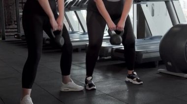 Dinamik bir çekim, iki iri yarı sporcuyu, şık bir spor salonunda güven içinde kettlebell çömelmesi yaparken yakalar. Hareketli spor kıyafetleri ve odaklanmış ifadeleri vücut pozitifliğinin ve gücünün ruhunu somutlaştırıyor.