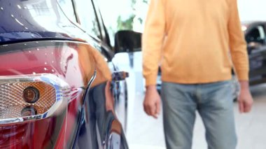 Neşeli, kıdemli, beyaz bir adam galerideki çarpıcı bir mor geçidin arka kapısını hevesle açıyor. Potansiyel bir alışveriş için heyecanını gösteriyor. Yakından çekilen ışık, parlak sergi salonunun atmosferini yansıtıyor.