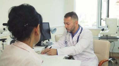 Parlak ve modern bir ofiste, nazik bir doktor genç bir bayanla görüşürken röntgen filmini dikkatle inceler. Atmosfer sakin ve profesyonel, ciddi konuşmalarında sağlık ve bakımın önemini vurguluyor.