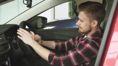 Şık sakallı genç bir adam modern bir arabada rahat bir şekilde oturur, direksiyonu kendine güvenen bir gülümsemeyle kavrar, otomotiv lüksünün cazibesini sergiler. Parlak iç mekan ve parlak gösterge paneli macera ve heyecan hissini yansıtıyor.