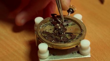 Bu büyüleyici makro çekimde, yetenekli bir saatçi titizlikle eski bir saatin karmaşık tekrarlayıcı mekanizmasına bir çark yerleştirir. Sıcak ahşap arka plan sahneyi güzelleştirir, hassasiyeti ve sanatsallığı vurgular.