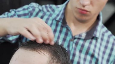 Odaklanmış bir kuaför, erkek bir müşterinin ıslak saçlarını ustalıkla tarar, modern bir berber dükkanında hassasiyet ve özen gösterir. Atmosfer canlı ve profesyonel, tımar sanatını ve berber ile berber arasındaki bağı vurguluyor.
