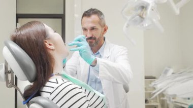 Neşeli genç bir kadın dişçi muayenesinden sonra kendinden emin bir şekilde kameraya ışıldarken olgun bir erkek dişçi gururla yanında duruyor. Parlak, modern diş sağlığı kliniği kurulumu sağlık ve canlılık atmosferini geliştirir.