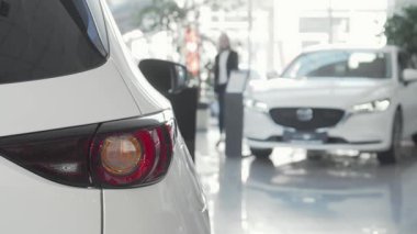Odaklanmış bir bayan müşteri parlak bir galeride parlak bir otomobili dikkatle inceliyor, ön planda parıldayan araba ışıkları dikkat çekiyor. Bulanık arka planda modern araçlar sergileniyor.