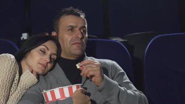 Yakışıklı, olgun bir adam kamerayı nazikçe kapatır, güzel karısı omzunda huzur içinde uyur, sinemada samimi ve romantik bir ortam yaratır. Bu samimi an, sevgi ve korumanın özünü yakalar.